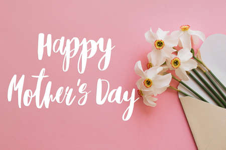 Happy mother's day greeting card. Happy mother's day text and white daffodils flowers blooming from envelope on pink paper flat lay. Stylish floral greetings. Handwritten lettering. Mothers dayの写真素材
