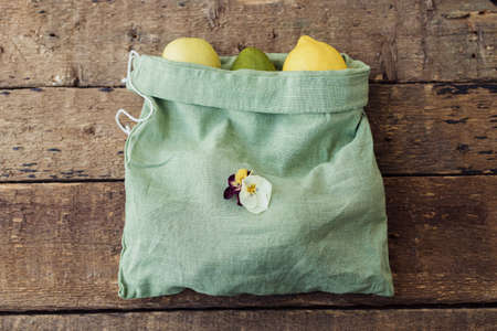 Fresh apples, avocado, lemons in eco cotton bag on rustic wooden table. Zero waste shopping concept....