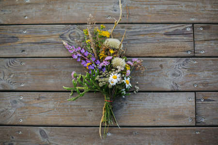 Beautiful bouquet of wildflowers on rustic wooden background. Summer vacation in countryside. Traveling in mountains and gathering wildflowers. Top view with space for textの写真素材
