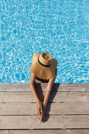 Beautiful tan woman in hat relaxing in pool water at wooden pier, enjoying summer vacation, top...