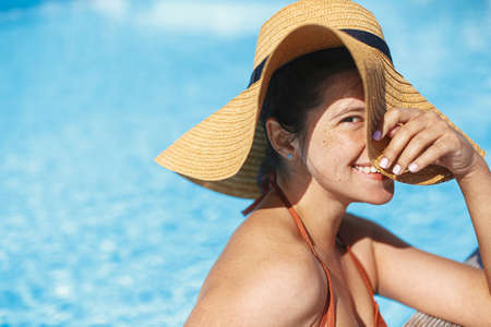 Beautiful happy carefree woman in hat relaxing in pool, enjoying summer vacation. Portrait of...