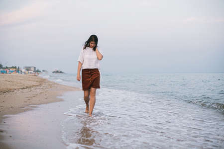 Carefree hipster woman walking barefoot on sandy beach with sea waves in the evening, enjoying...