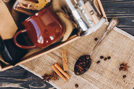 Gift box with coffee set. Coffee in spoon, cinnamon, anise on burlap on wooden table at box with...