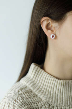 Beautiful stylish woman with cute earring with red heart, cropped view. Fashionable female in...
