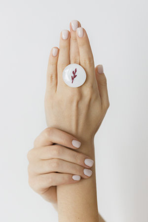 Stylish modern white round ring on beautiful hands on white background. Unusual fashionable fused...