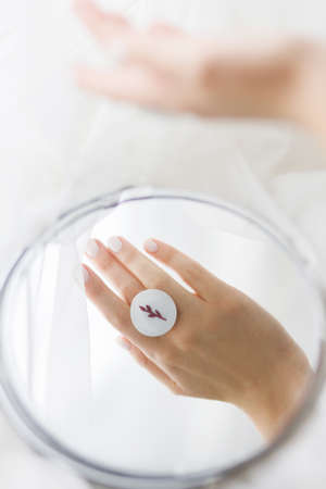 Stylish modern white round ring on beautiful hand reflected in mirror on background of soft white...