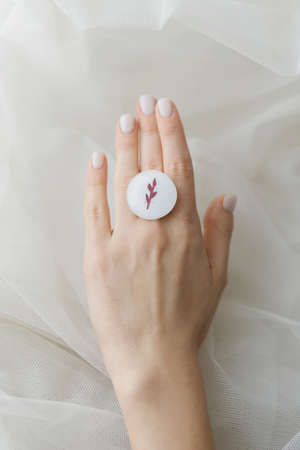 Stylish modern white round ring on beautiful hand on background of soft white tulle. Unusual...