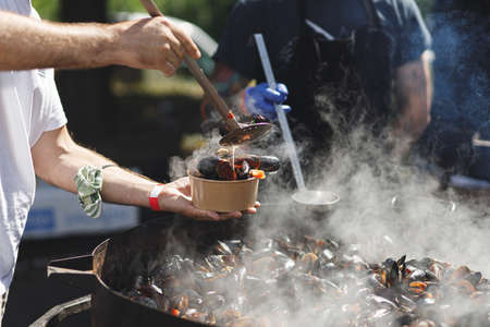 Chef putting delicious boiled mussels in take away box, cooking seafood at street food festival....