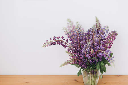 Beautiful lupine bouquet on wooden table in white room. Gathering countryside wildflowers, rural still life. Purple lupine flowersの写真素材
