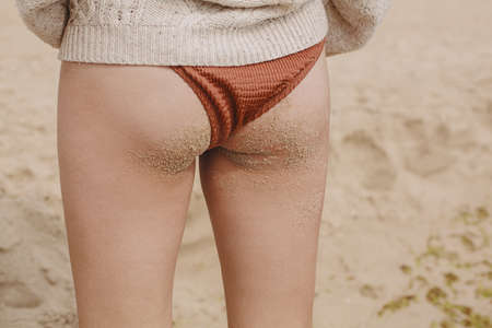 Woman buttocks and tanned legs in sand on background of sandy beach, lifestyle. Stylish young female...
