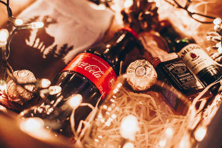 Lviv, Ukraine - December 1, 2017: Stylish socks, coca cola, jack daniels and jameson whiskey, glass cup and candy on straw in gift box with christmas lights. Gift box for birthday, fathers dayのeditorial素材