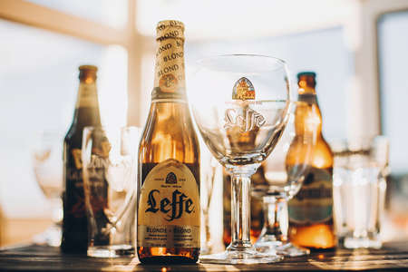 Lviv, Ukraine - December 1, 2017: Leffe beer bottle and glass in warm sunny light on background of Guinness and Hoegaarden beers on countertop. Hoegaarden beer and glass with brand logo and labelのeditorial素材