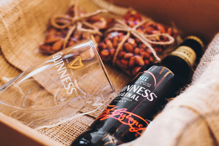 Lviv, Ukraine - December 1, 2017: Guinness beer bottle, glass cup and salted nuts snacks on burlap in gift box. Stylish gift box for man birthday, fathers day. Guinness beer and mug with labelのeditorial素材
