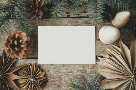 Empty greeting card and christmas paper stars, wooden tree, pine branches and cones on rustic background. Christmas card mock up flat lay. Space for text. Seasons greetings template. Plastic freeの写真素材