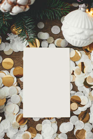 Christmas card mock up. Empty greeting card and christmas vintage baubles, decorations, confetti and pine branches on rustic wood. Flat lay. Space for text. Seasons greetings template