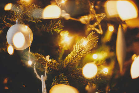 Modern christmas tree ornaments, white baubles and golden christmas lights bokeh close up. Space for text. Atmospheric festive decorated scandinavian room in night. Stylish christmas decorの写真素材