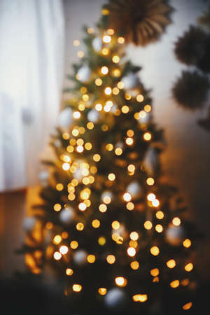 Golden Christmas tree lights defocused in evening festive room. Christmas background, glowing illumination bokeh. Atmospheric christmas eve. Merry Christmas and Happy holidaysの写真素材