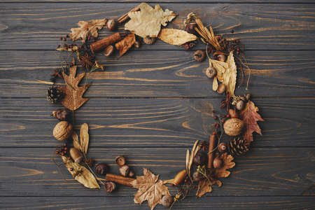 Autumn wreath flat lay. Autumn leaves, berries, nuts, anise, acorns in circle on dark wood. Rustic autumnal wreath with dried herbs. Happy Thanksgiving and Hello autumnの写真素材