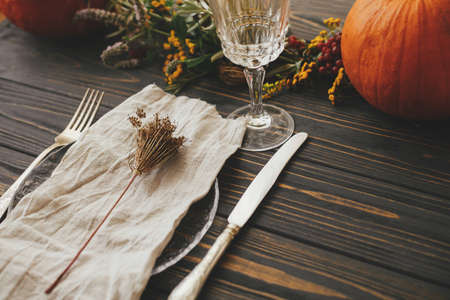 Modern plate with vintage cutlery, linen napkin, herb on wooden table with pumpkins and autumn flowers arrangement. Eco friendly Thanksgiving dinner table setting. Rustic autumn wedding cateringの写真素材