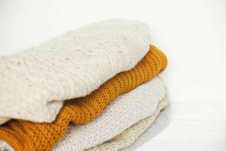 Cozy knitted sweaters. Pile of white, yellow and beige knit sweaters close up in white scandinavian room. Hello autumn. Stylish wardrobe for cold seasonの写真素材