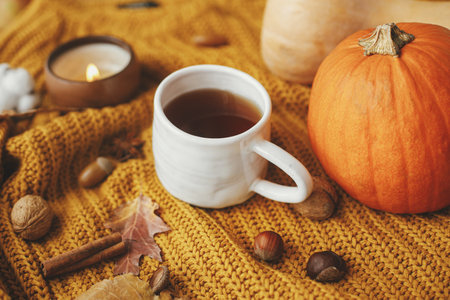 Warm cup of tea on yellow knitted sweater with pumpkins, autumn leaves, burning candle. Cozy autumn slow living. Happy Thanksgiving. Hello fall seasonの写真素材