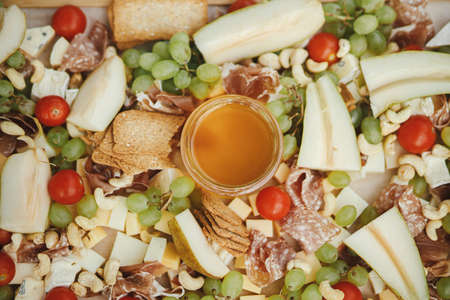 Cheese board with maasdam, bree, cheddar, prosciutto, salami, honey, grapes, pears and cherry tomatoes on wood. Charcuterie board and Antipasto. Italian appetizers for outdoor gathering partyの写真素材