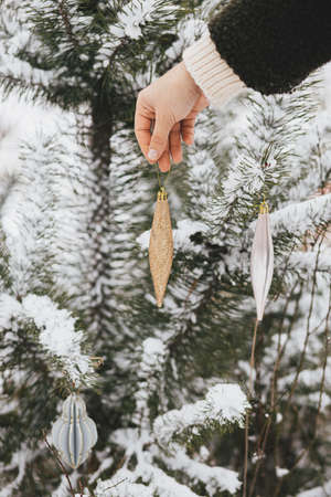 Hand decorating pine tree branches with modern bauble. Decorating christmas tree in snow outdoors. Preparation for winter holidays in countryside. Merry Christmas! Space for textの写真素材