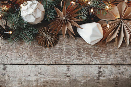 Stylish christmas ornaments, paper stars, fir branches, cones and lights border on rustic old wooden background. Top view with space for text. Season's greeting card. Merry Christmas!の写真素材