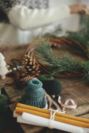 Stylish festive christmas candle on background of woman in cozy sweater making christmas wreath on rustic wooden background. Space for text. Happy holidays. Festive winter workshopの写真素材