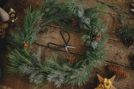 Christmas rustic wreath. Stylish christmas wreath on rustic wooden background with pine cones, scissors, candles, ornaments, top view. Happy holidays. Festive winter workshopの写真素材