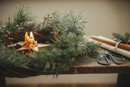 Christmas advent. Stylish burning star candle in christmas wreath with spruce branches and berries on rustic wooden background. Merry Christmas and Happy holidays. Atmospheric moody imageの写真素材