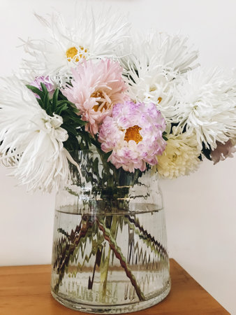 Beautiful autumn flowers in modern glass vase on wooden table. Asters and chrysanthemums flowers in modern room close up. Hello autumn concept, floral arrangement on homeの写真素材