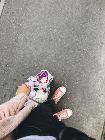 Top view of stylish hipster woman holding bag with bunch of autumn flowers. Hello autumn concept, buying flowers in reusable bag. Female legs in pink sneakersの写真素材