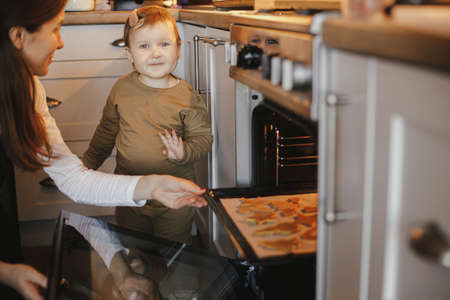 Cute little daughter and mother baking christmas gingerbread cookies in modern scandinavian kitchen....