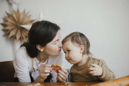 Cute daughter and mother making together christmas cookies on messy table. Adorable toddler girl helper with mom cutting dough for gingerbread cookies. Family preparations for xmas holidaysの写真素材