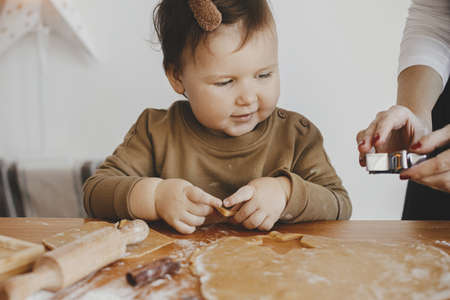 Adorable little daughter with mother making together christmas gingerbread cookies on messy wooden...