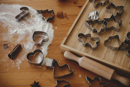 Metal cookie cutters, rolling pin and flour on wooden table for gingerbread cookies. Christmas...