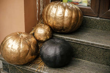Golden and black pumpkins in city street, festive holiday decor of storefronts and buildings. Halloween modern decoration outdoor. Happy halloween. Autumn market in town, painted pumpkinの写真素材