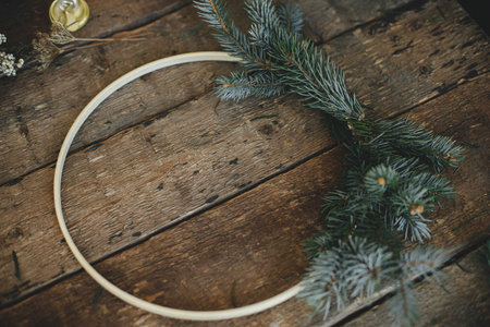 Making modern christmas wreath. Minimalist boho wreath with fir branches, herbs, round wooden hoop on rustic table. Atmospheric moody image. Winter holidays preparation.の写真素材