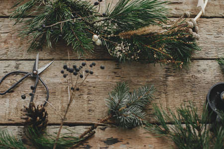Modern christmas wreath with spruce branches, herbs, scissors, candle on rustic wood. Merry...