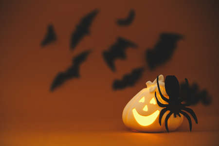Happy Halloween. Glowing Jack o lantern pumpkin decoration with spider on orange background with flying black bats. Halloween background. Greeting card with space for text.の写真素材
