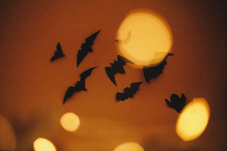 Happy Halloween. Bats flying on dark orange background with magical lights bokeh. Atmospheric...