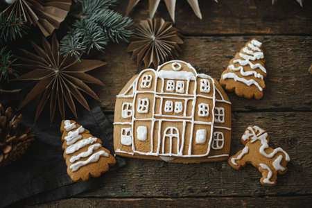 Merry Christmas and Happy Holidays! Christmas gingerbread cookies with icing on rustic wooden table with ornaments. Making gingerbread house with frosting. Atmospheric moody image.の写真素材