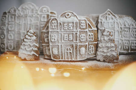 Christmas gingerbread houses and tree in snow on rustic wooden table with golden lights. Christmas cookies village scene. Atmospheric moody image. Winter holiday traditions. Merry Christmas!の写真素材