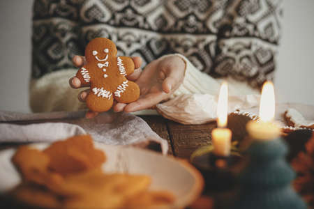 Hands holding decorated gingerbread man christmas cookie on background of rustic table with napkin,...
