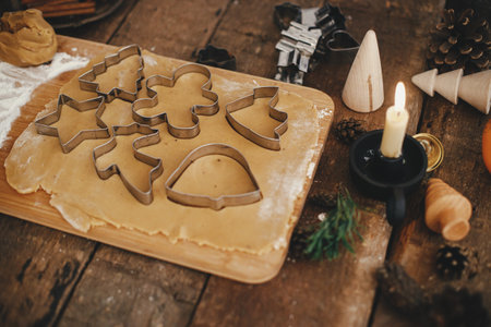 Gingerbread dough with christmas metal cutters on wooden board. Atmospheric Moody image. Making traditional christmas gingerbread cookies on rustic table with candle, spices, decorationsの写真素材