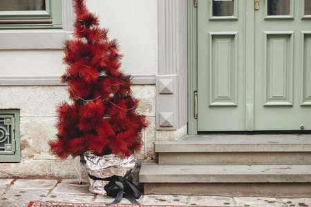Modern red christmas tree at building front of store entrance. Stylish Christmas festive street decor in european city for winter holidays. Happy Holidays!の写真素材