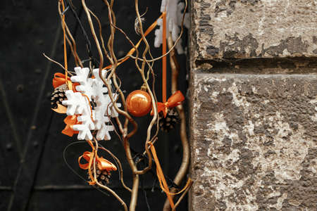 Stylish simple christmas decoration with branch, orange ornaments and snowflake on old building....
