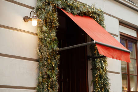 Stylish spruce branches and lights, christmas decoration of door in european city street. Festive christmas decor for winter holidays. Holiday winter fair.の写真素材