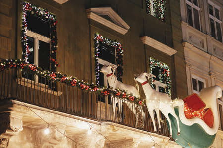 Stylish santa sleigh ride with reindeers and christmas branches in lights illumination on balcony of building in evening. Atmospheric magic time, winter holidays. Merry Christmas!の写真素材